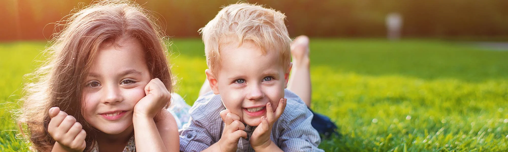 boy and girl toddler laying on the grass with their faces facing camera and smiling